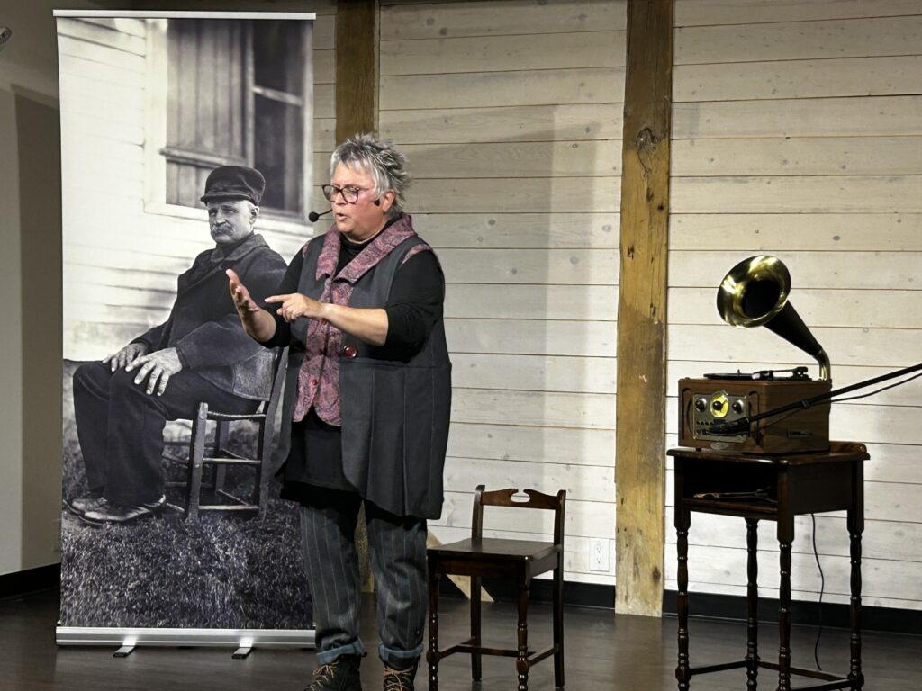 Conférencière présentant une activité culturelle devant une photographie historique et un gramophone ancien.