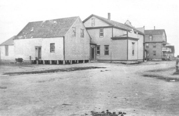 Photographie historique en noir et blanc de bâtiments anciens et d’une rue du village à Lamèque.