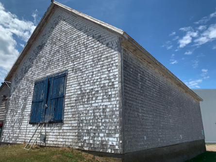 Bâtiment patrimonial en bois avec grandes portes bleues sous un ciel ensoleillé à Lamèque.